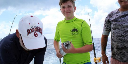 boy in green shirt holding a baracuda on a deep sea fishing trip in Cozumel
